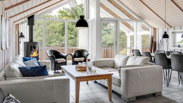Een ruime woonkamer met een open haard, comfortabele zithoek en grote ramen met uitzicht op de omgeving.