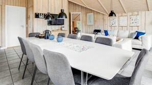 Een ruime eetruimte met een lange tafel, grijze stoelen en hanglampen.