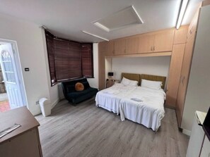 Une chambre avec deux lits, un bureau, une chaise et une fenêtre avec des stores.