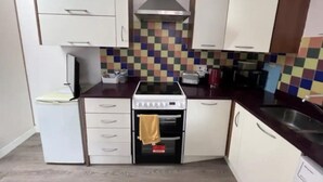 A compact kitchen with white cabinets, a colorful checkered backsplash, a built-in oven, and a microwave. - Inviting 1-bed Apartment in Ilford (Ilford)