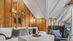 A cozy room with a white sofa, a grey armchair, and a white coffee table. There is a wooden shelf with decorative items and a hanging light fixture. - "Magga" - 3.2km from the sea by Interhome (Rømø)