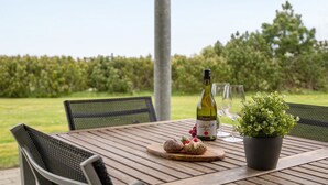 Una mesa de madera con una botella de vino, copas, una planta y una tabla de madera con pan y fruta.