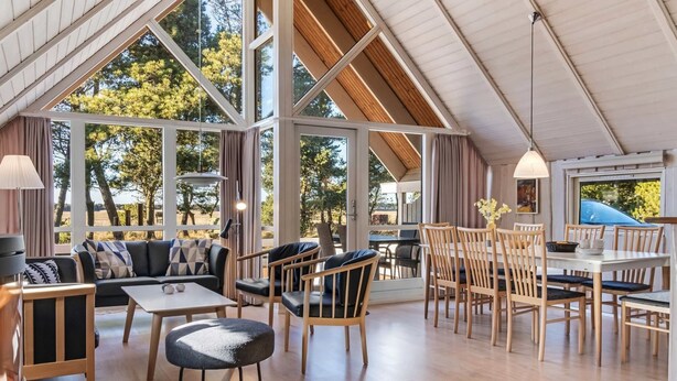 A spacious room with a high ceiling, large windows, and a mix of seating areas including a sofa and chairs.