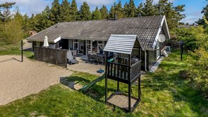 Una casa de playa con patio, mobiliario exterior y zona de juegos.