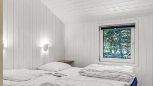 Un dormitorio con cama, mesita de noche, lámpara de pared y ventana con vista a árboles.