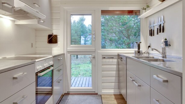 Eine moderne Küche mit weißen Schränken, einer doppelten Spüle und einem Fenster mit Blick auf eine Holzterrasse.