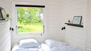 Ein Schlafzimmer mit zwei Betten, einem Fenster mit Blick ins Grüne und einem Regal mit einem Bild und einer Pflanze.