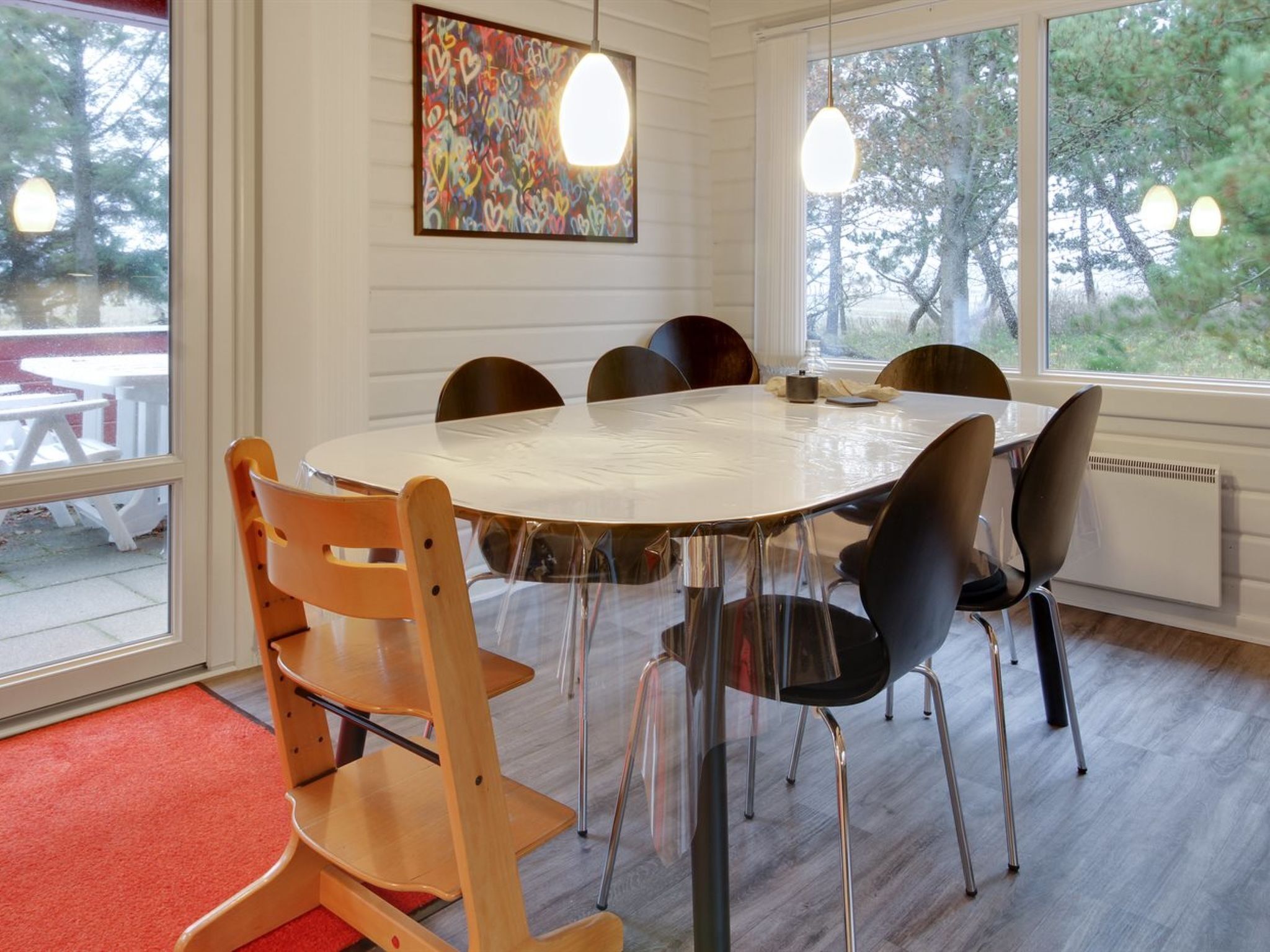 Een ronde tafel met stoelen, een kleurrijk abstract schilderij en grote ramen met uitzicht op bomen.