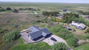 Une grande maison dotée d’une vaste terrasse et d’une piscine, entourée d’un immense champ et de quelques bâtiments plus petits.