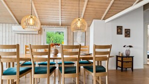 Un coin repas avec des chaises et une table en bois, deux luminaires suspendus et une vue sur la verdure à l’extérieur.