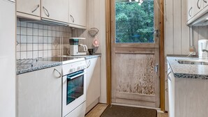 A compact kitchen with white cabinets, a built-in oven, a coffee maker, and a window with a view of trees. - "Falki" - 2.5km from the sea by Interhome (Rømø)