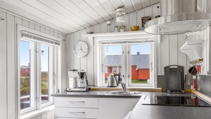 Moderni keittiö, jossa on valkoiset kaapit, sisäänrakennettu liesi ja kahvinkeitin.