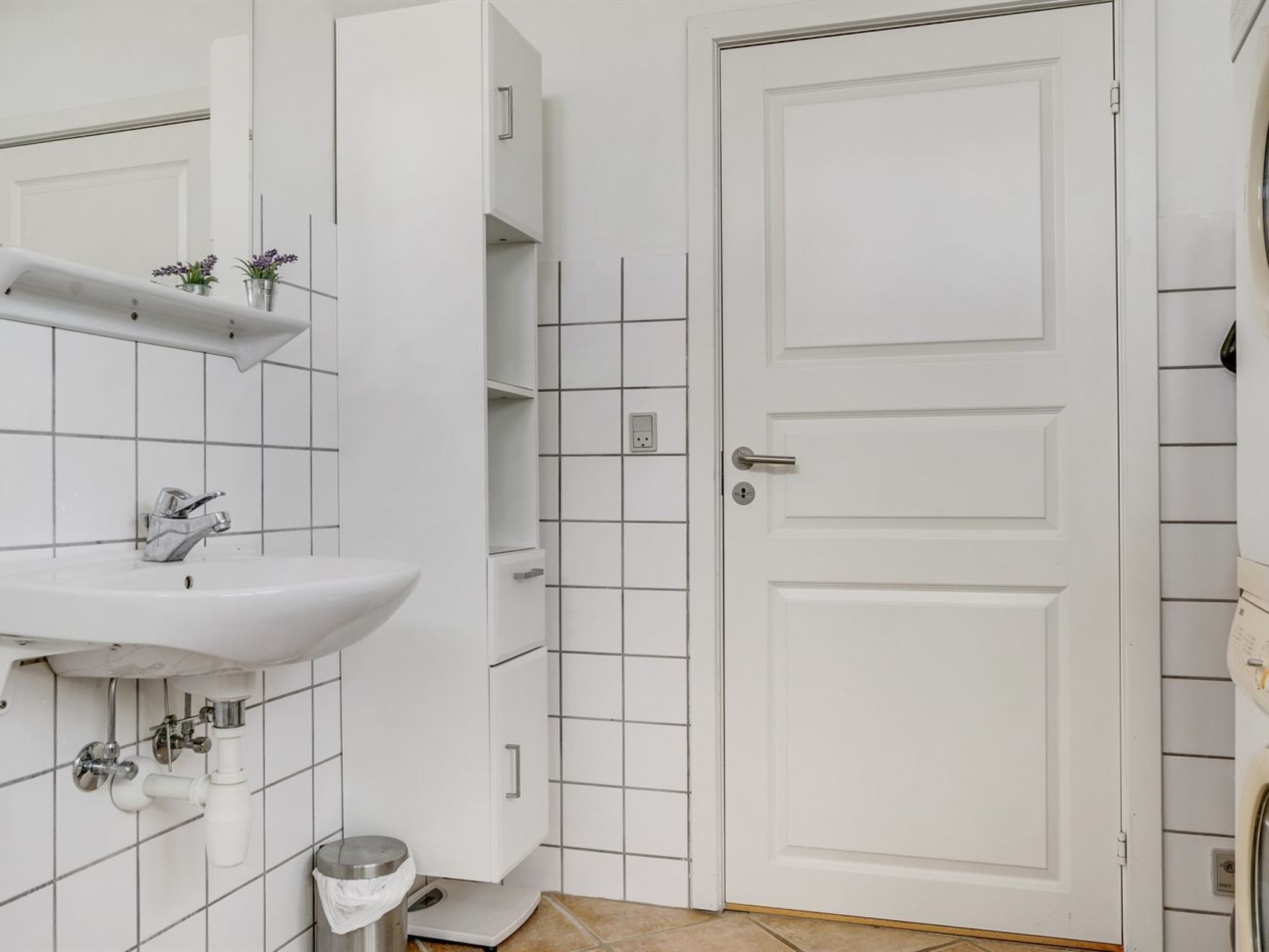 A bathroom with a white sink, a mirror, a white door, and a tiled wall.