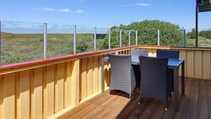 A wooden deck with two wicker chairs and a table, overlooking a grassy landscape.