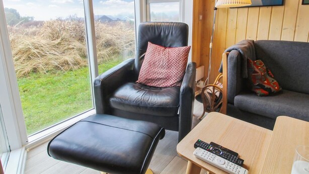 A modern living room with a leather armchair, a grey sofa, and a wooden coffee table. A remote control is on the table, and a lamp is on the floor.