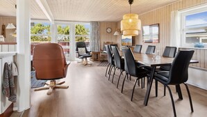 A spacious dining area with a wooden ceiling, a large dining table surrounded by chairs, and a view of the outdoors through a large window.