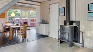 A modern kitchen with a wood stove, a dining area with chairs and a table, and a view through large windows.