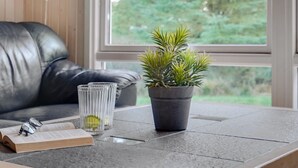 A modern room with a leather sofa, a table with a book, glasses, and a potted plant.