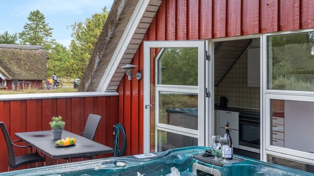 A hot tub in a red building with a table and chairs outside.