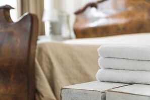 A neatly made bed with a beige bedspread and a stack of white towels on a wooden nightstand.