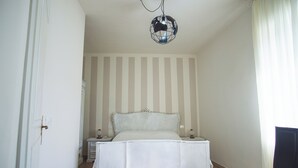 Quarto com cama, mesa de cabeceira, cadeira e luminária suspensa.