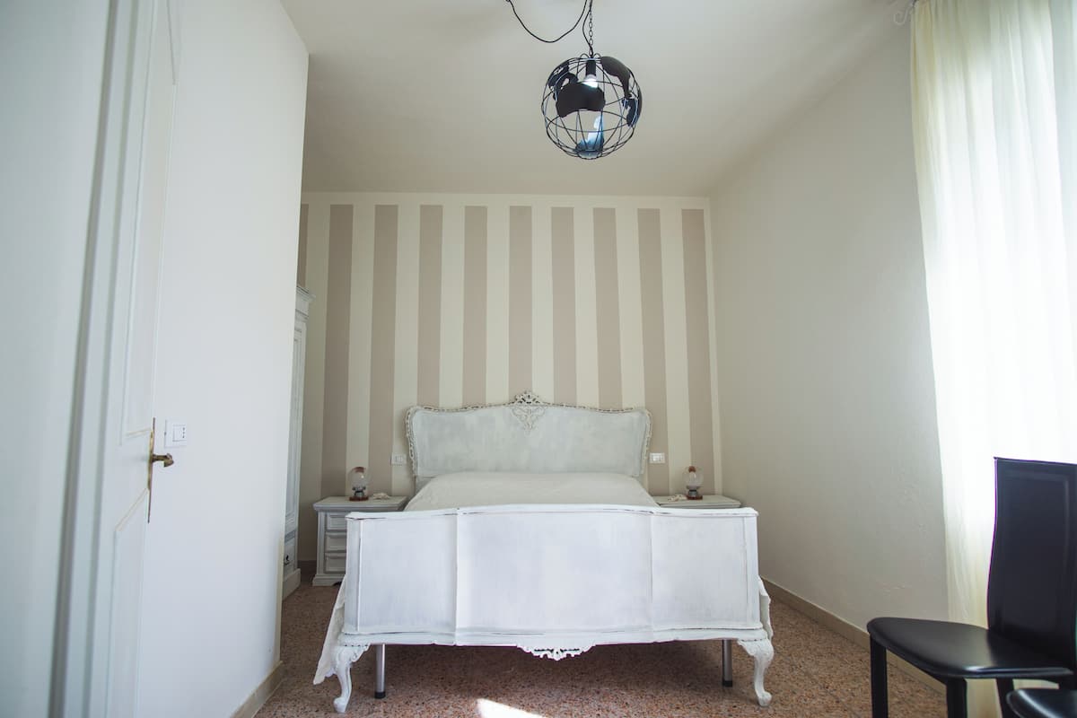 A bedroom with a bed, a nightstand, a chair, and a hanging light fixture.