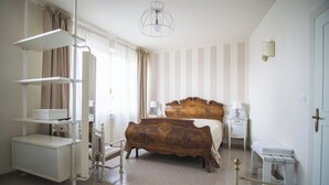 Quarto com cama de madeira, mesa de cabeceira branca, criado-mudo, estante e luminária suspensa.