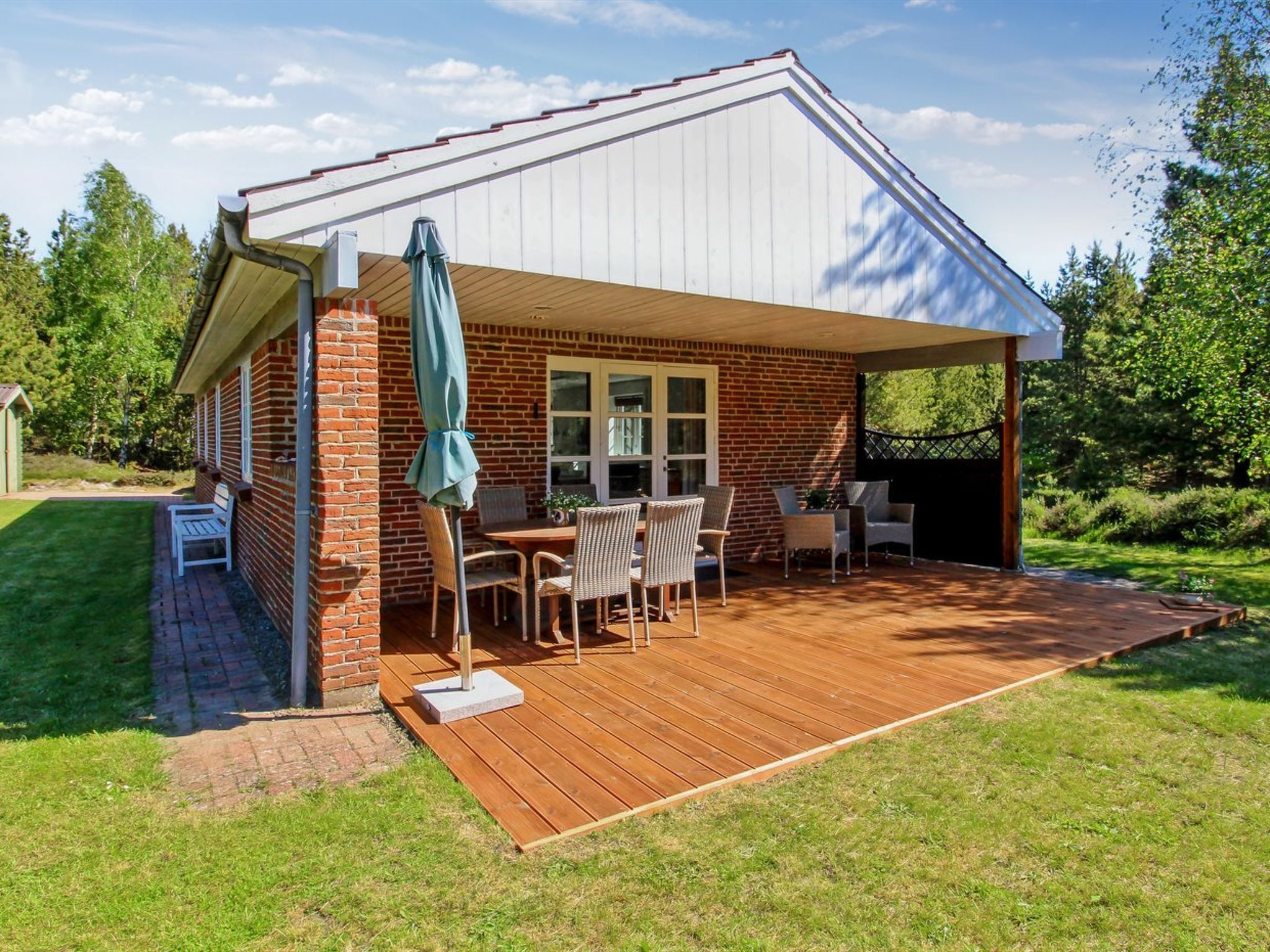 Um alpendre coberto com fachada de tijolos, deck de madeira e mobiliário para exterior.