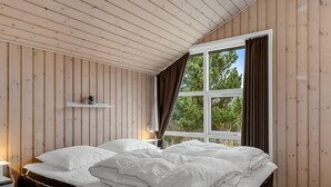A bedroom with a wooden sloped ceiling, a large window with curtains, a bedside table with a lamp, and a bed with white bedding. - "Sakulfuer" - 2.5km from the sea by Interhome (Rømø)