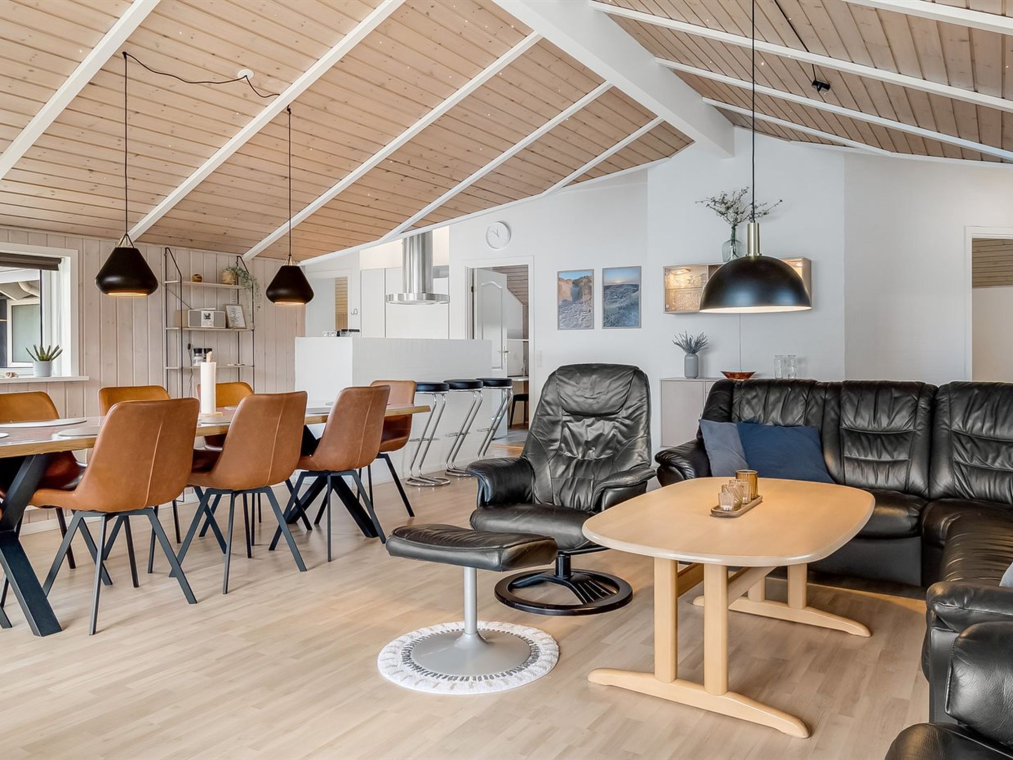 A modern living room with a dining area, leather sofas, a round coffee table, and pendant lighting.