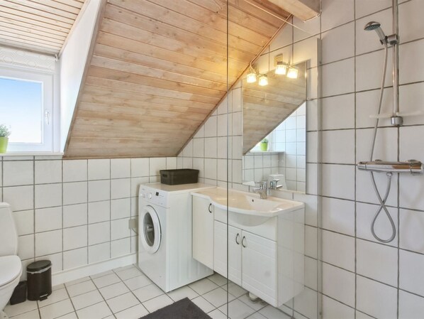 A modern bathroom with a washing machine, sink, and shower.