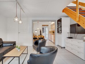 A modern living room with a sofa, coffee table, and chairs. There is a kitchen area with cabinets and a dining table. A staircase leads to an upper level. - "Paula" - 2.3km from the sea by Interhome (Rømø)