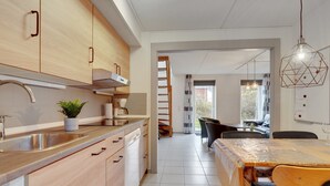 Een moderne keuken met houten kastjes, een roestvrijstalen spoelbak en een eethoek met een tafel en stoelen.