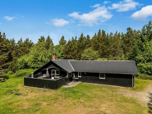 A black metal building with a flat roof, a chimney, and a covered outdoor area with a table and chairs.