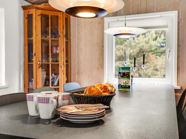 A kitchen with a dining table, a basket of bread, and a window with a view of greenery.