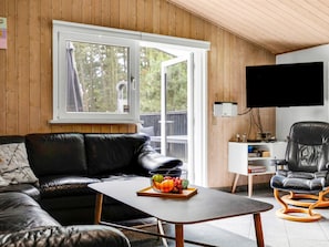 A modern living room with a leather sofa, a coffee table with fruit, a TV, and a wooden ceiling.