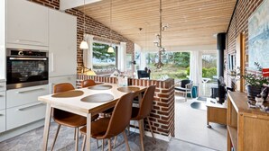 Una cocina moderna con pared de ladrillo decorativa, un área de comedor con mesa y sillas de madera, y vistas al exterior.