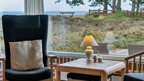Una habitación con vista a la playa, una silla, una mesa con lámpara y una ventana.