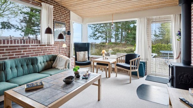 Una sala de estar acogedora con pared de ladrillo, techo de madera y ventanas amplias que dan al exterior.