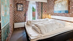 Un dormitorio con pared de ladrillo, cama, ventana y obras de arte.