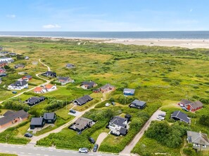 An aerial view of a coastal residential area with houses, roads, and a beach in the background.