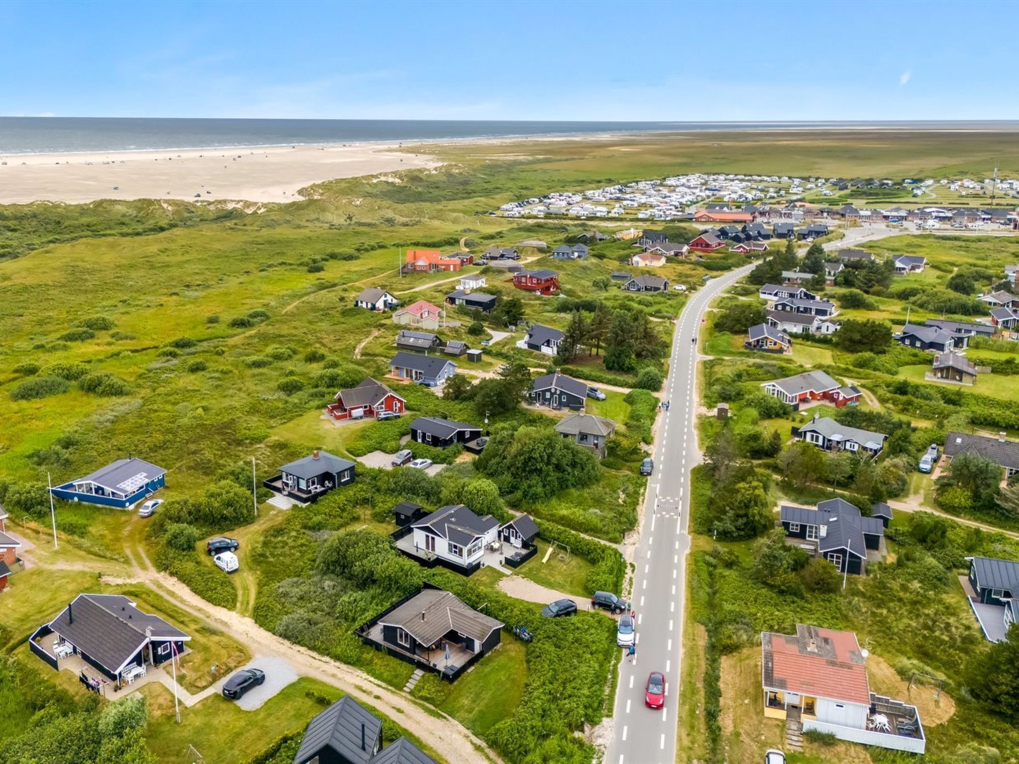Luftaufnahme einer Küstenwohngegend mit Häusern, einer Straße und einem Strand im Hintergrund.