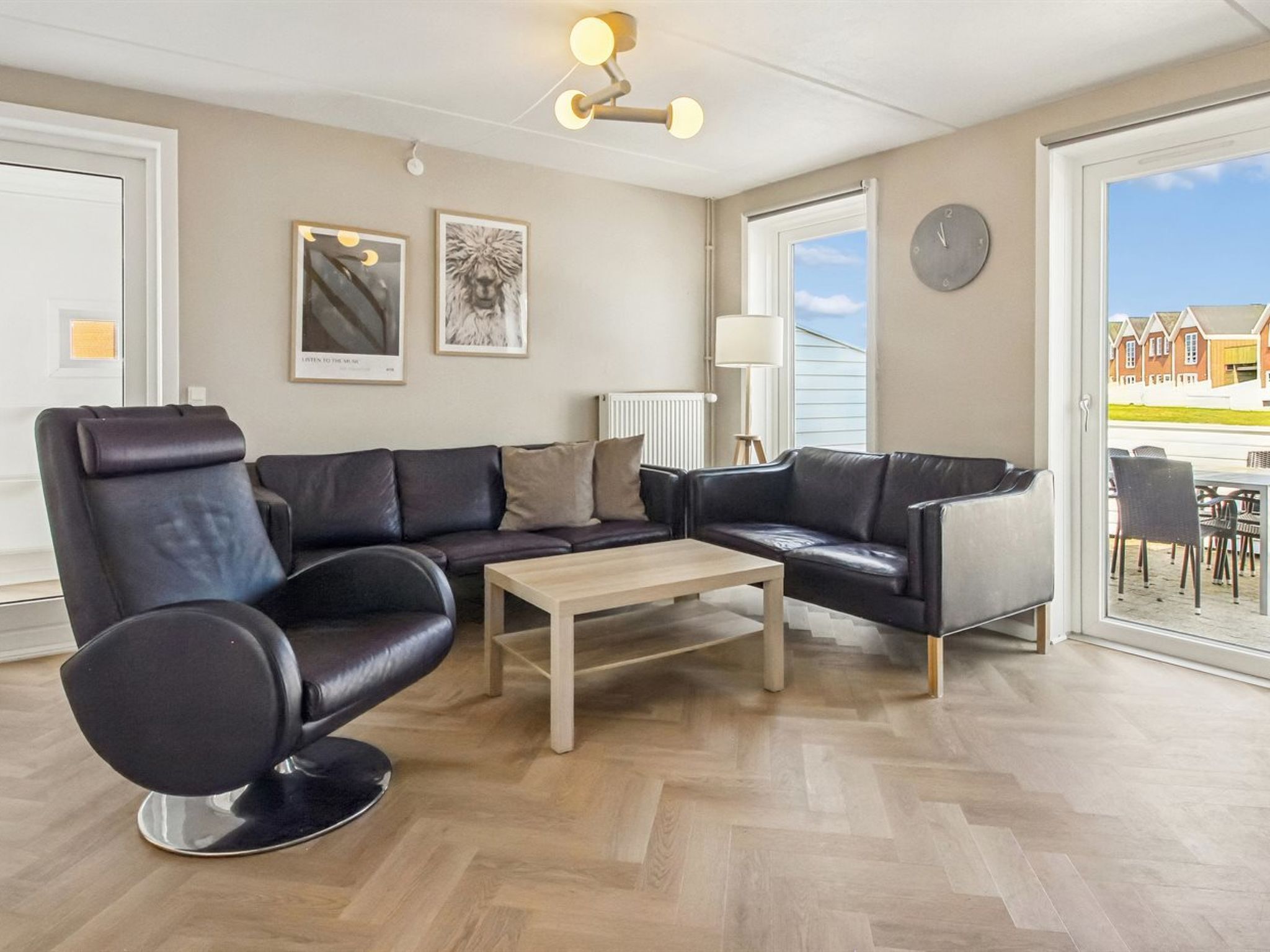 A modern living room with leather sofas, a wooden coffee table, and a large window offering a view of houses.