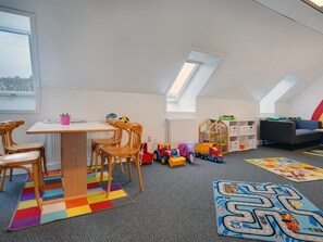 Habitación ideal para niños, con mesa, sillas, un espacio de juegos con juguetes y una alfombra colorida.