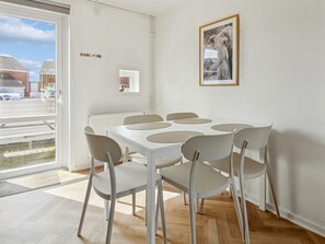 A dining area with a white table and chairs, a framed picture on the wall, and a view of the outside.