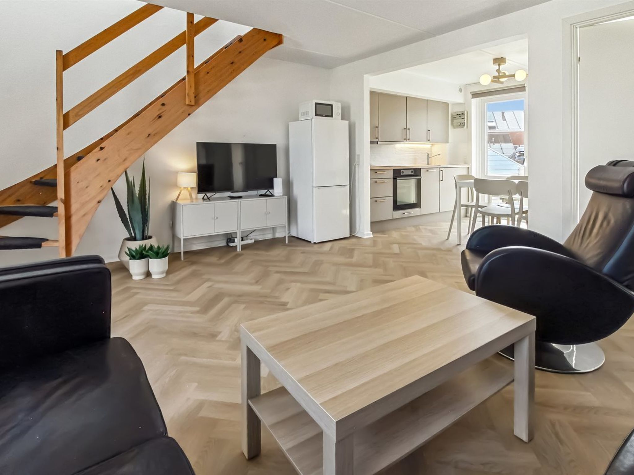 Una sala de estar moderna con una escalera de madera, un televisor de pantalla plana, un refrigerador blanco y un comedor con vistas.