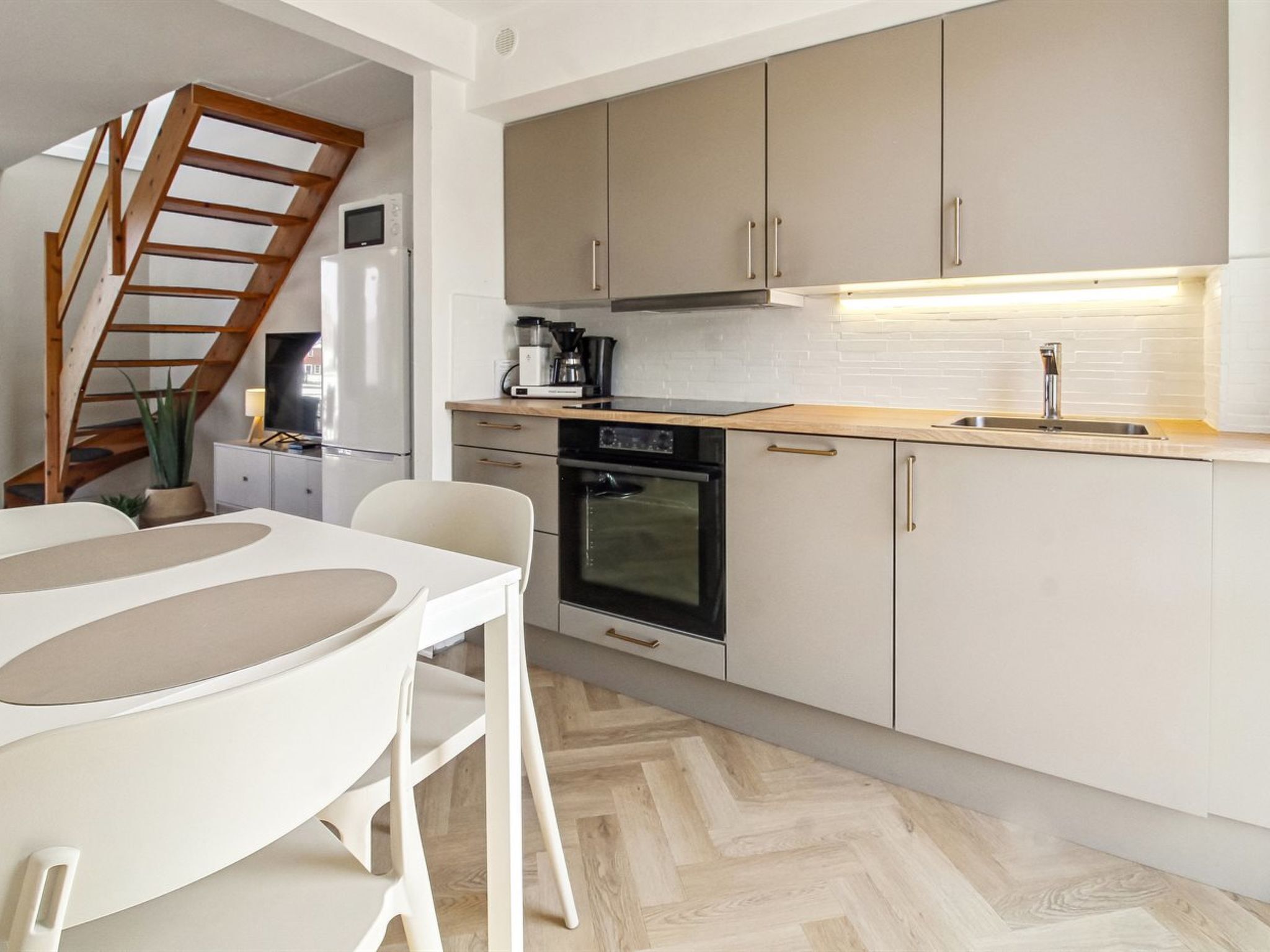 Eine moderne Küche mit Fischgrätparkett, einem eingebauten Ofen und einer Holztreppe.