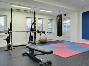 Un gimnasio con banco, equipo de levantamiento de pesas, saco de boxeo y una pelota de ejercicios grande.