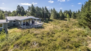 Et hus med terrasse, omgivet af tæt skov og græsarealer.