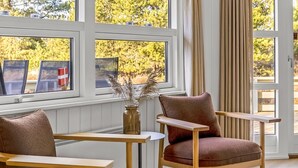 Et værelse med store vinduer, en stol, et lille bord og en vase med tørrede planter.